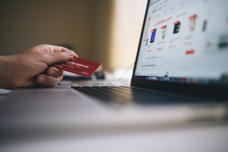 A hand holding a credit card in front of a laptop showing an online sale page, illustrating a customer reacting to a price change