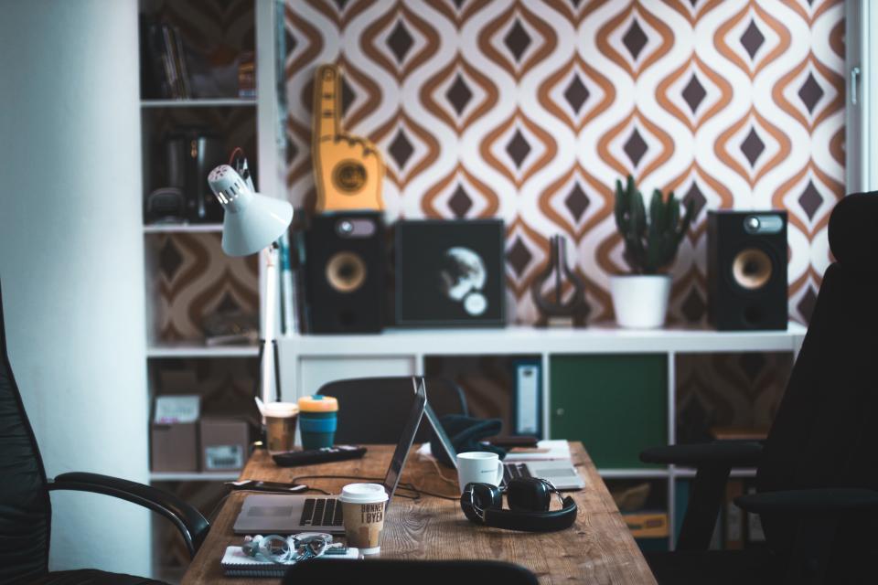 A creative workspace desk with a laptop, coffee, and speakers, illustrating choosing the right AI image tool for a small catalog