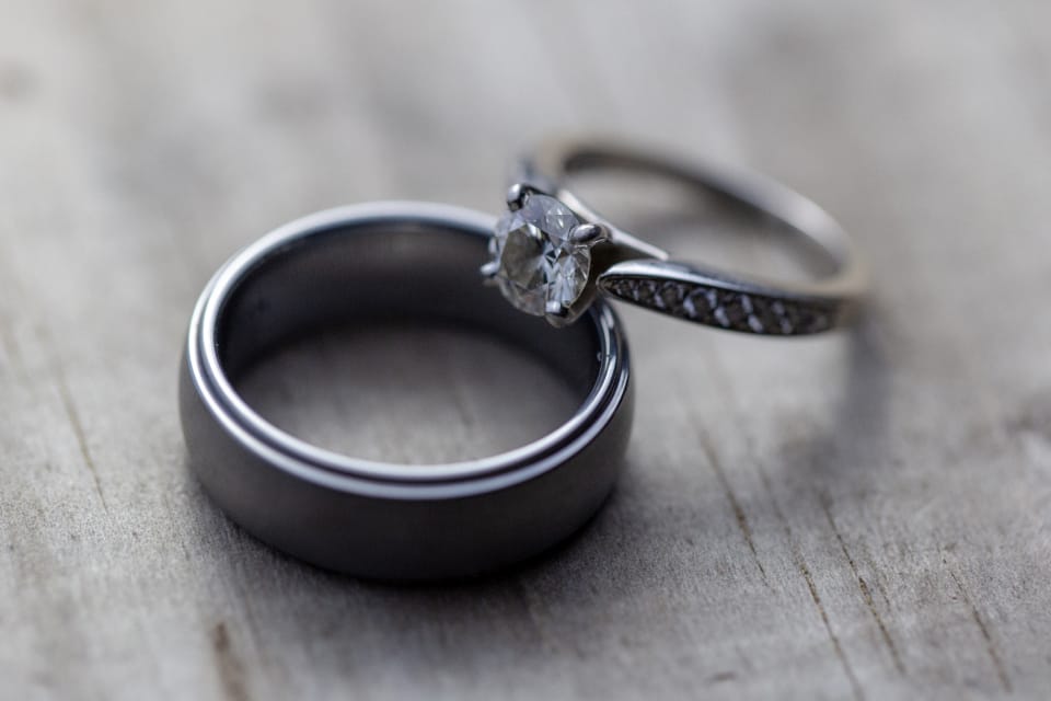 Two reflective wedding rings with a diamond on a wood surface, illustrating where AI product photography still fails on metallic and glass surfaces